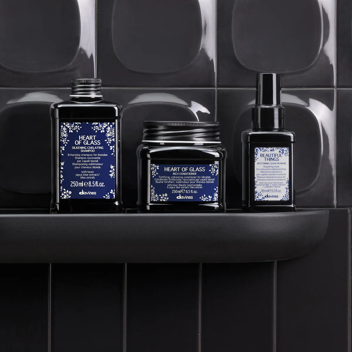 Heart of Glass Silkening Shampoo tillsammans med kompletterande hårvårdsprodukter i svarta förpackningar placerade på en svart hylla mot mörka kakelväggar, miljövänliga hårvårdsprodukter för vård och styling.