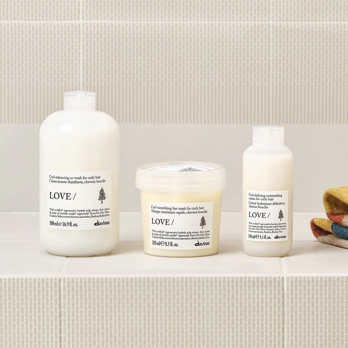 Tre miljövänliga hårvårdsprodukter från Davines med fokus på Love Curl Enhancing Co-Wash för definierade och återfuktade lockar, placerade på beige kakel.