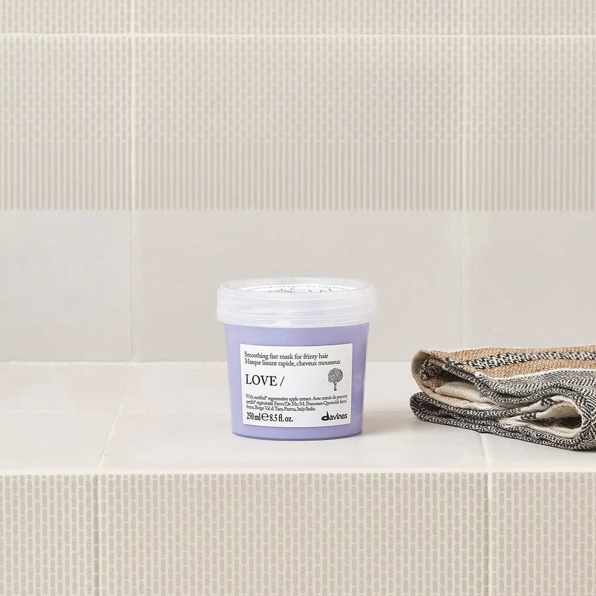 Love Smoothing Fast Mask i en lila burk för hårinpackning, placerad på ett badrumsgolv bredvid hopvikt handduk, miljövänliga hårvårdsprodukter.