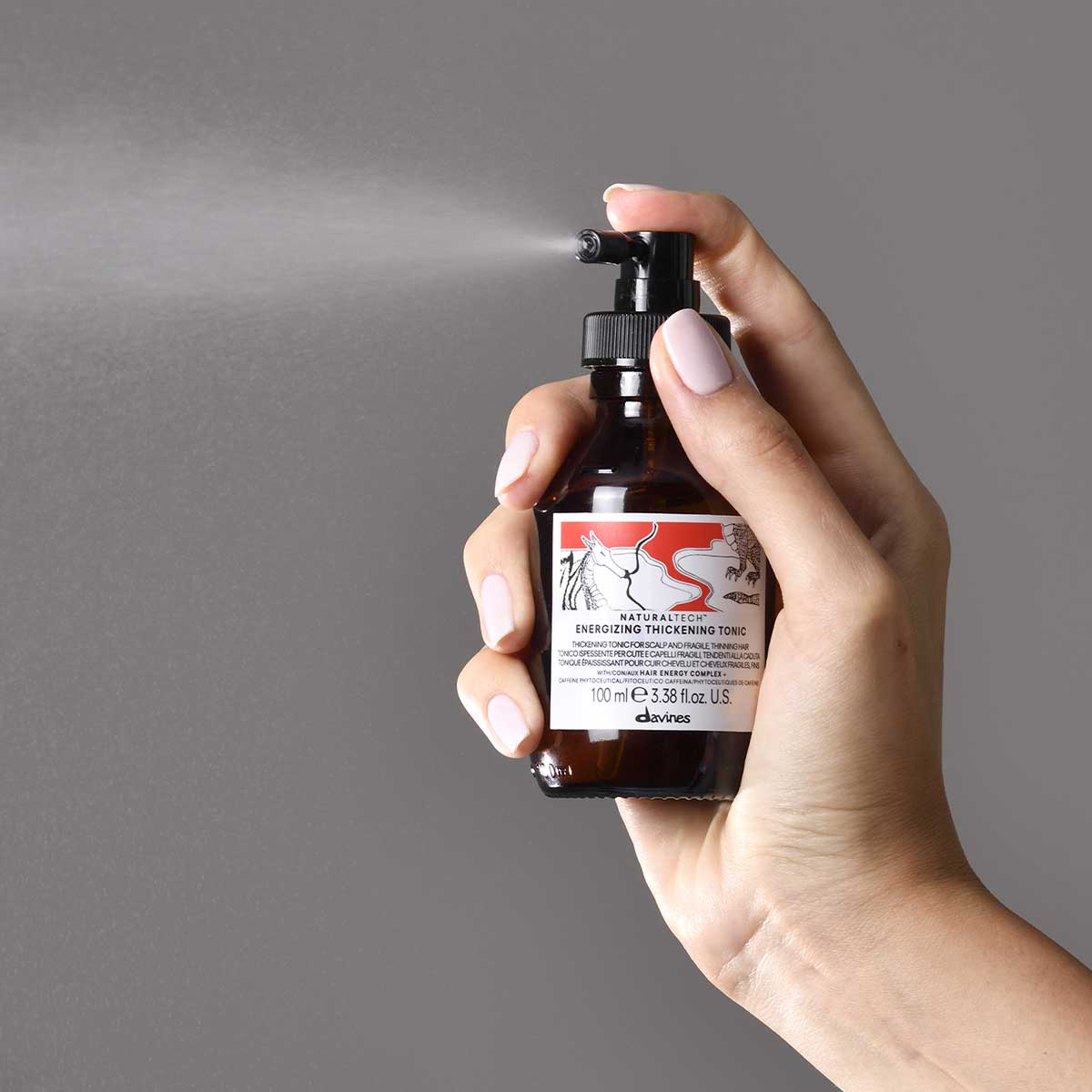Hand håller en sprayflaska och applicerar Naturaltech Energizing Thickening Tonic för att ge volym och textur till håret.
