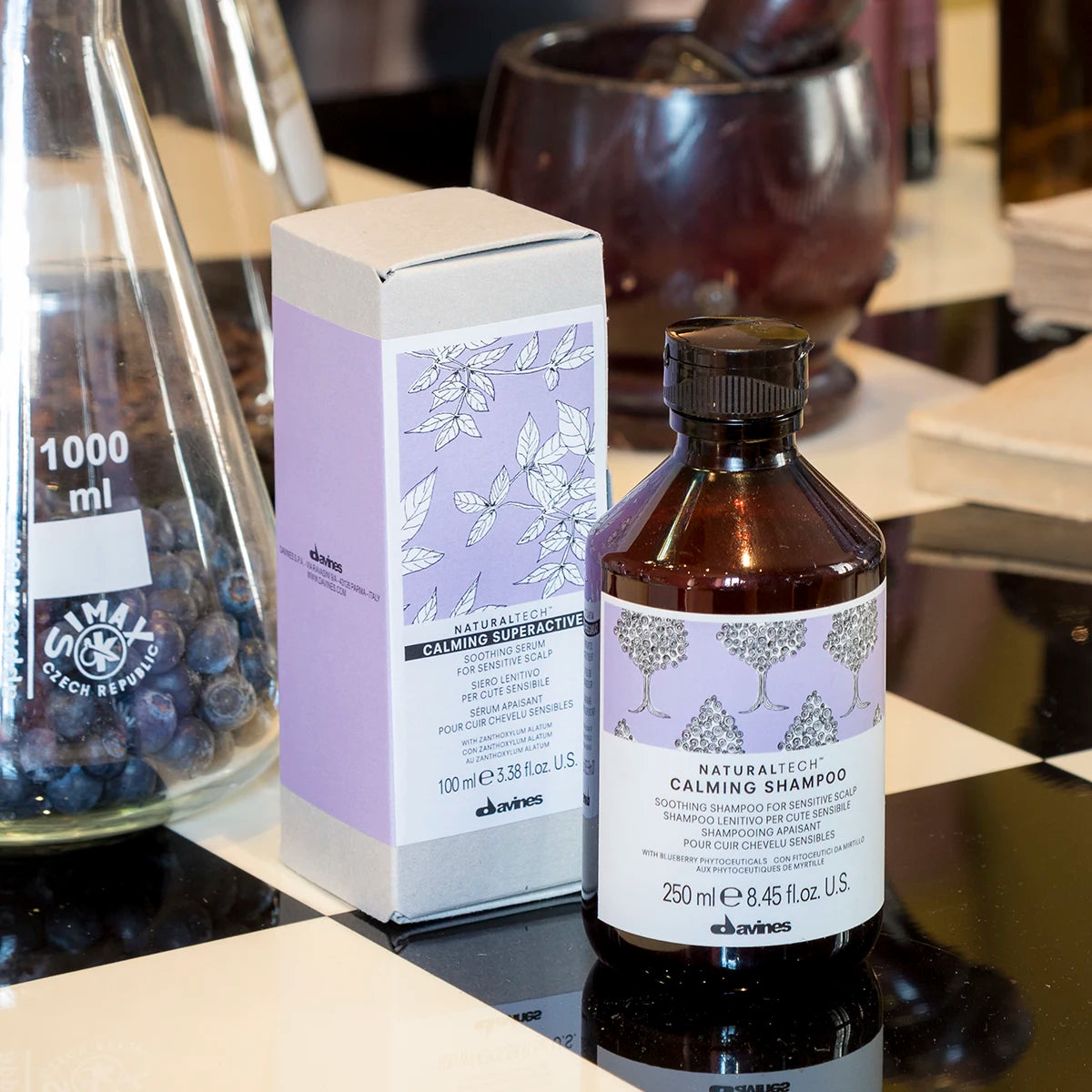 Naturaltech Calming Shampoo i brun flaska med lila etikett placerad bredvid en kartong med matchande design på svartvit bordsskiva.